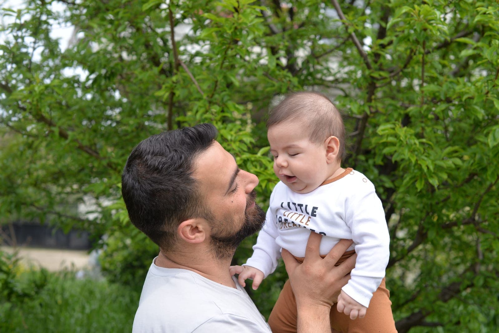 A father holding his baby son outdoors among greenery