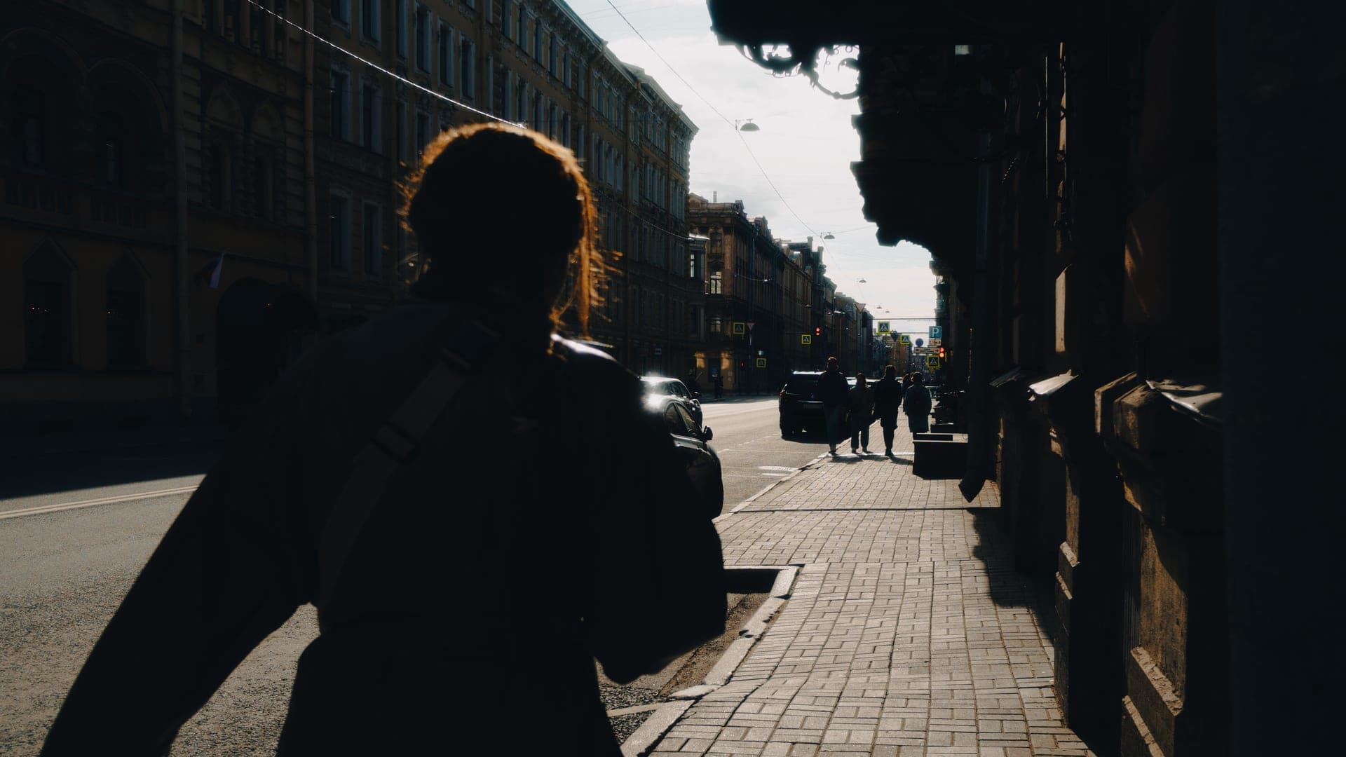 A person walking down a sunlit street carrying a backpack