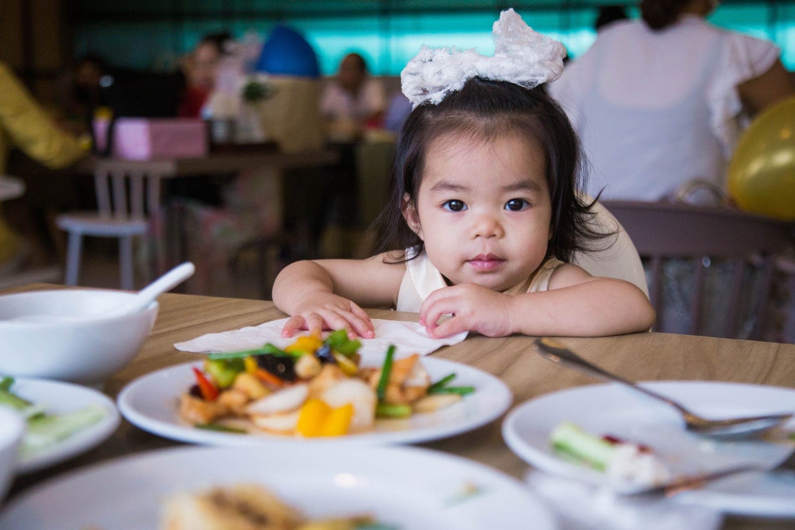 A toddler at a restaurant table with several dishes in front of her