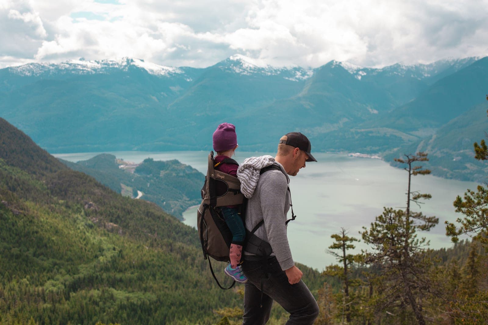 A parent carrying a child on a mountain trail