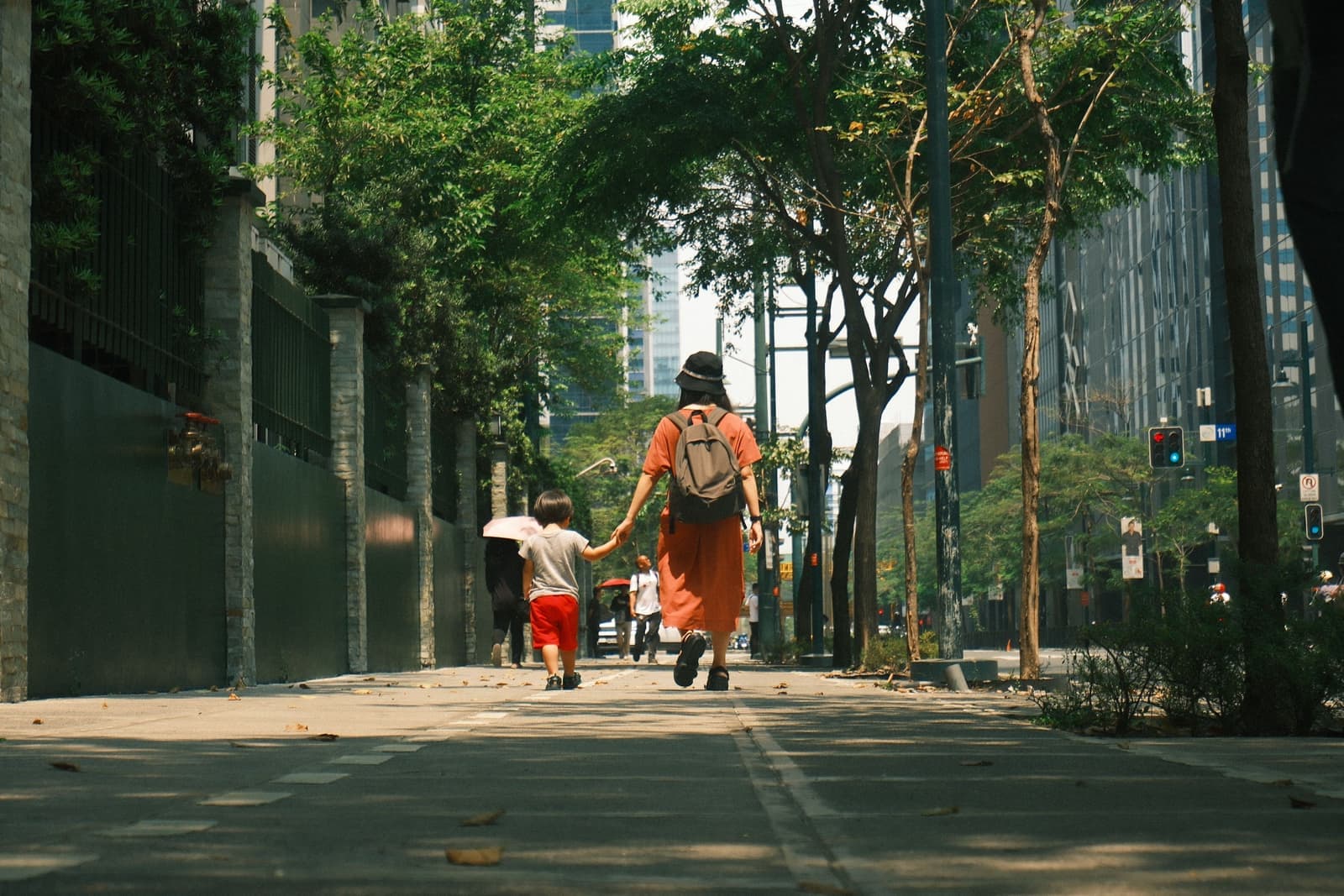 A parent and child walking hand in hand down a sunny city street