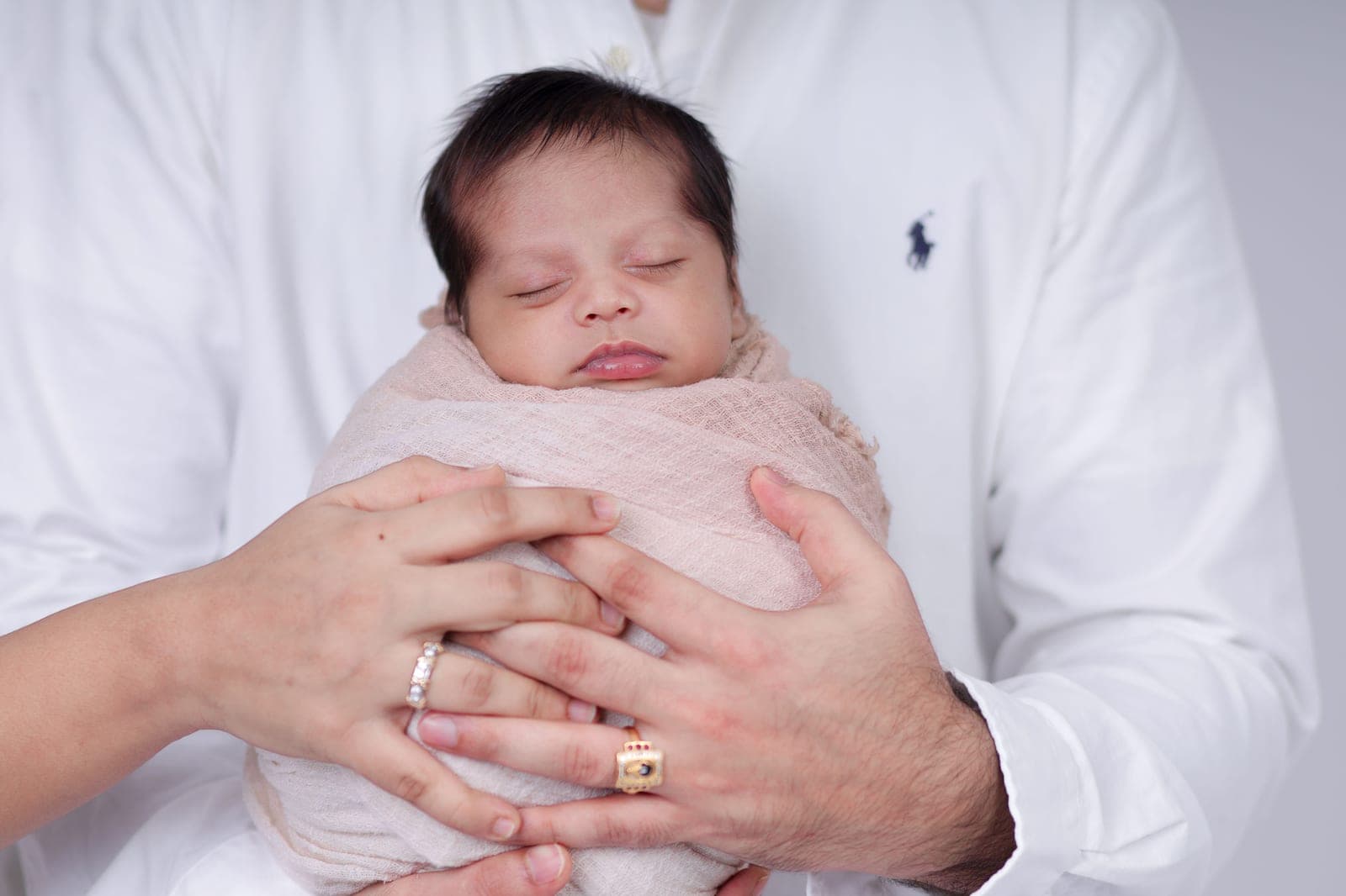Parents holding a sleeping newborn wrapped in soft fabric