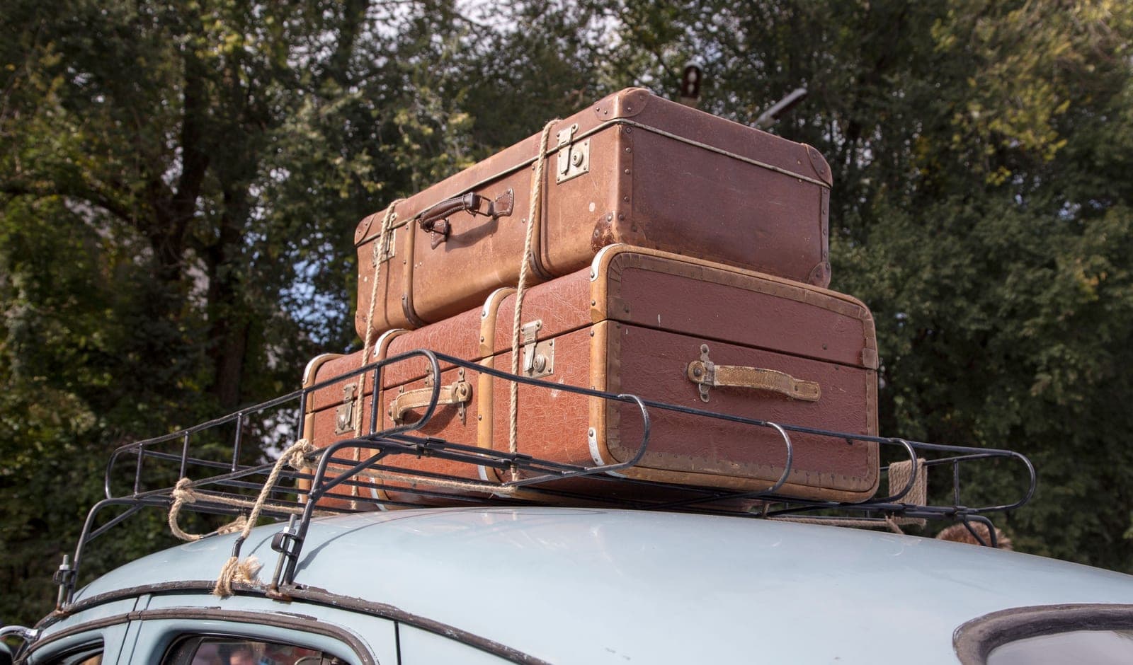 Suitcases strapped to the roof rack of a car packed for a road trip