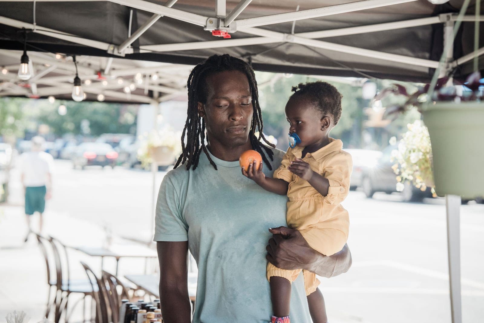 A father holding his daughter on his hip under a market awning